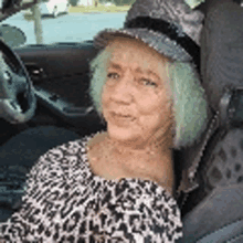 a woman with green hair is sitting in a car wearing a hat and a leopard print shirt .