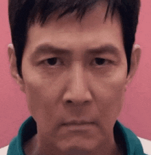 a close up of a man 's face wearing a green shirt against a pink background .