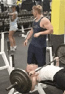 a man is lifting a barbell on a bench in a gym while a woman looks on .