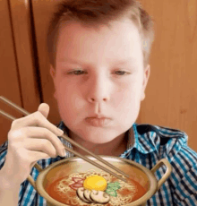 a boy with chopsticks is eating a bowl of ramen