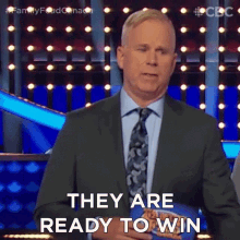 a man in a suit and tie is standing in front of a sign that says they are ready to win .