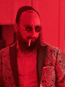 a man with a beard wearing sunglasses and a paisley jacket smoking a cigarette