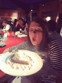 a woman in a striped shirt is holding a plate of food in front of a sign that says ' primor '