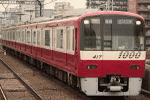 a red and white train is going down the tracks in a city .