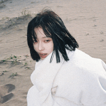 a woman with short black hair is wrapped in a white blanket on a sandy beach