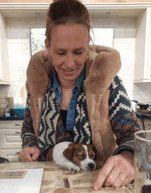 a woman sits at a table with a small brown and white dog sleeping on the table