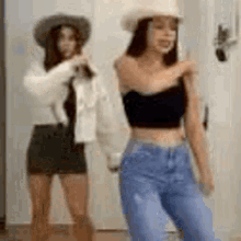 two women are standing next to each other in front of a door . one of the women is wearing a cowboy hat .