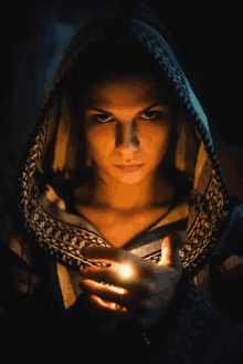 a woman in a hooded sweater holds a lit candle in her hands