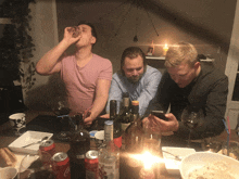 three men are sitting at a table with bottles of wine and a can of coca cola