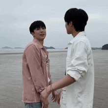 two men holding hands on a beach with one wearing a shirt that says ' i love you ' on the front