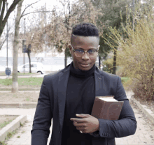 a man wearing glasses and a black jacket holds a brown book