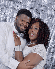 a man and a woman pose for a picture with a silver background