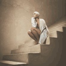 a woman squatting down on a set of stairs looking up