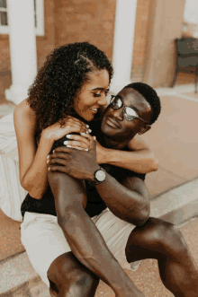 a man wearing sunglasses and a watch is carrying a woman on his shoulders