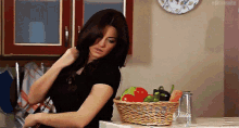 a woman adjusts her hair in front of a basket of vegetables and a glass with the word juice on it