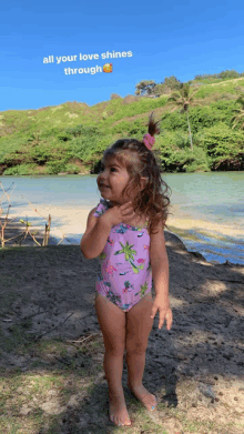 a little girl in a pink swimsuit stands on the beach with the words all your love shines through above her