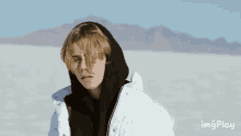 a young man wearing a white jacket and a black hoodie is standing in a snowy field .