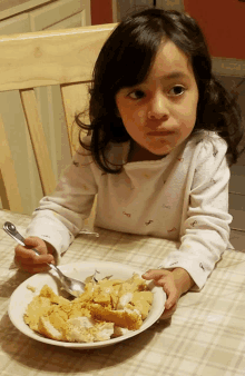 a little girl is sitting at a table with a plate of food and a spoon