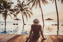 a man in a hat sits on a wooden deck near a pool