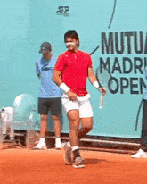 a man in a red shirt is holding a tennis racket in front of a sign that says mutua madrid open