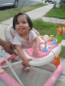 a baby girl is sitting in a pink walker and smiling