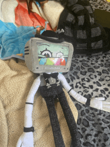 a stuffed toy with a television head is laying on a bed with a leopard print blanket