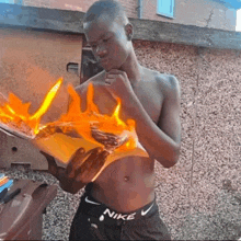 a shirtless young man is holding a piece of paper that is on fire .