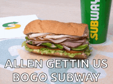 a subway sandwich sits next to a green subway cup