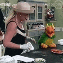 a woman wearing a hat and gloves is standing in a kitchen with a stuffed animal on the counter .