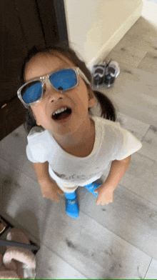 a little girl wearing blue sunglasses and a white shirt