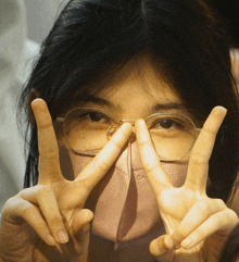 a woman wearing glasses and a pink face mask making a peace sign