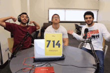 three men are sitting at a table with a laptop and a sign that says the podcast on it