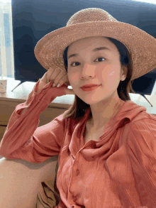 a woman wearing a straw hat and a pink shirt is sitting in front of a tv