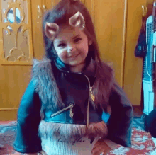 a little girl wearing a cat mask and a fur vest is smiling .