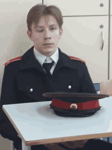 a man in a military uniform sits at a desk with a red hat on it