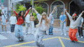 a group of people are dancing on a street in front of a building with a sign that says ' no smoking '