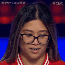 a close up of a woman wearing glasses and a red shirt with the words family feud canada behind her