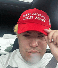 a man wearing a red make america great again hat smoking a cigarette