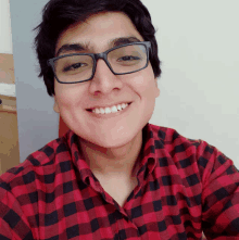 a young man wearing glasses and a red and black plaid shirt smiles