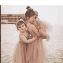 two little girls in pink dresses are standing next to each other on a beach .