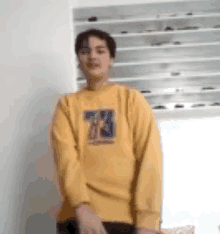 a young man wearing a yellow sweatshirt is standing in a room .