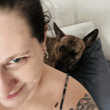 a woman with a tattoo on her arm looks at the camera with a dog in the background