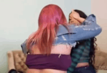 two women are hugging each other on a couch . one of the women has pink hair .