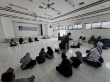 a group of people are sitting in a circle in a room with a banner on the wall that says ' selamat datang '