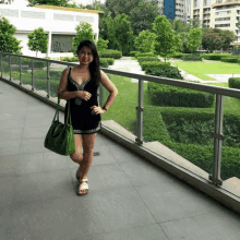 a woman in a black dress is standing on a balcony with a green purse