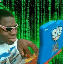 a man wearing sunglasses is using a shs laptop in front of a matrix background .