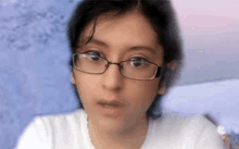 a girl wearing glasses and a white shirt is looking at the camera .