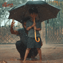 a man kneeling down with a child holding an umbrella in the rain with the word escape on the fence behind them