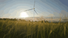 a wind turbine in a grassy field with the sun behind it