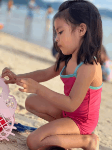 a little girl in a pink swimsuit is playing in the sand on the beach